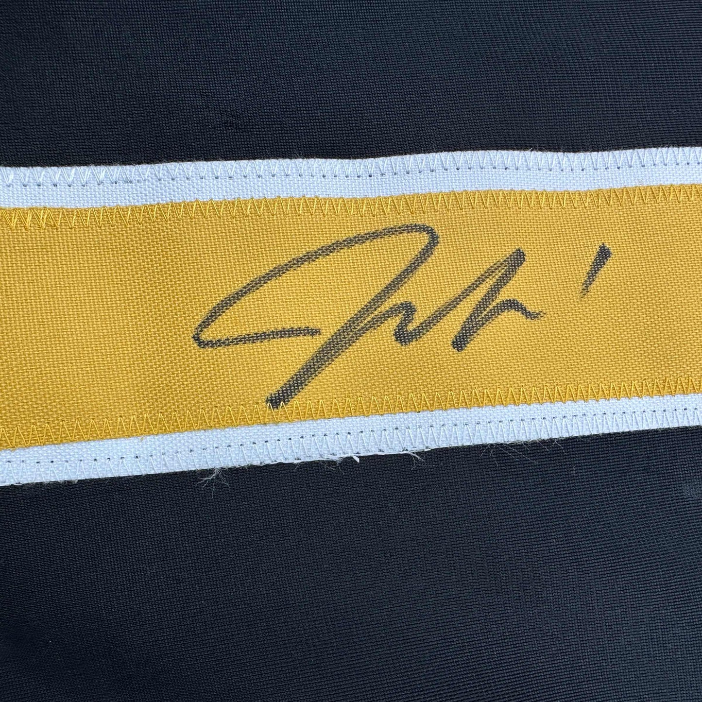 Close-up of handwritten signature on yellow stripe of black, white, and gold hockey jersey.