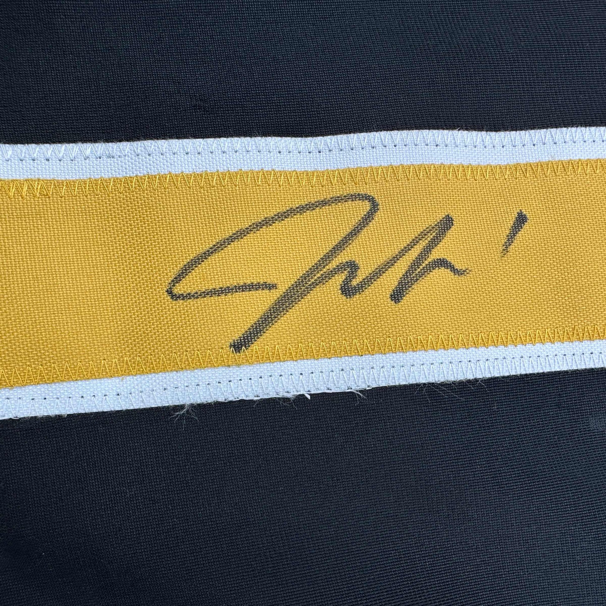 Close-up of handwritten signature on yellow stripe of black, white, and gold hockey jersey.