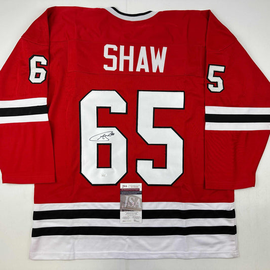 Red Chicago Blackhawks hockey jersey number 65 with Shaw name and autograph, displaying JSA authentication certificate attached at bottom.