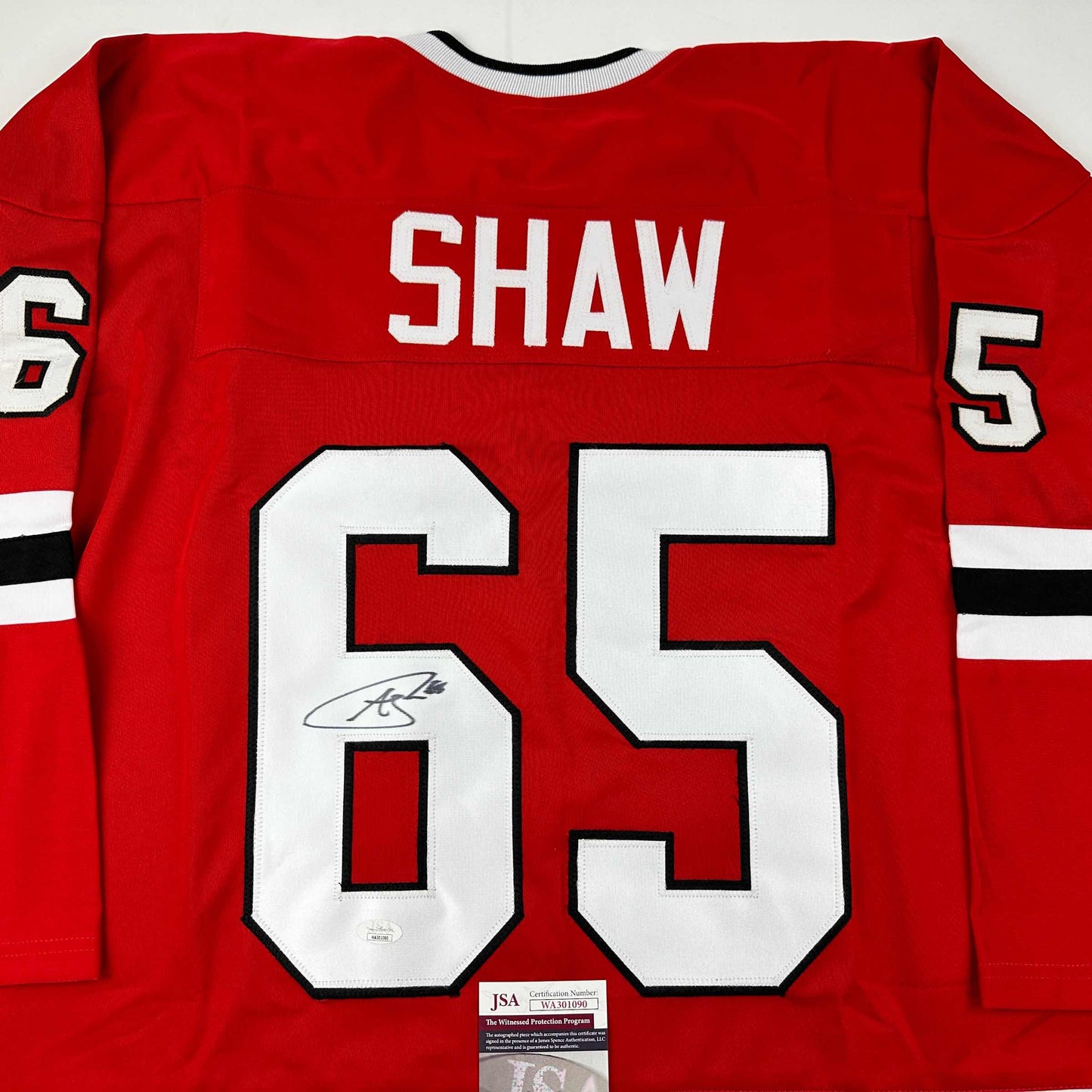 Back view of red Chicago hockey jersey number 65 with "SHAW" nameplate and autographed signature, JSA certificate visible at bottom.