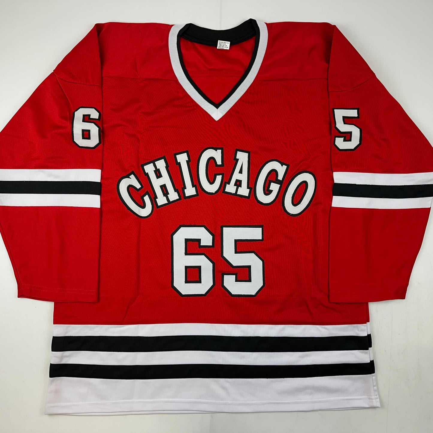 Red Chicago hockey jersey with white and black striping, displaying number 65 and "CHICAGO" text, laid flat on white background.