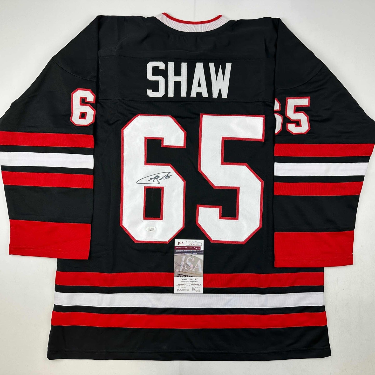 Signed Chicago Blackhawks jersey number 65 with Shaw name plate displayed flat showing back, red and black striped design with JSA authentication certificate.