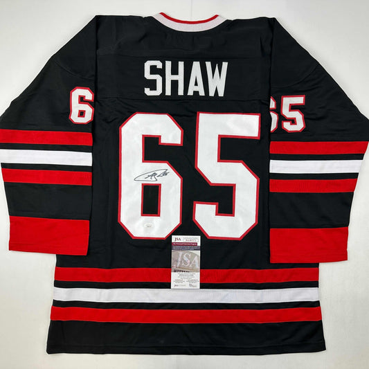 Signed Chicago Blackhawks jersey number 65 with Shaw name plate displayed flat showing back, red and black striped design with JSA authentication certificate.