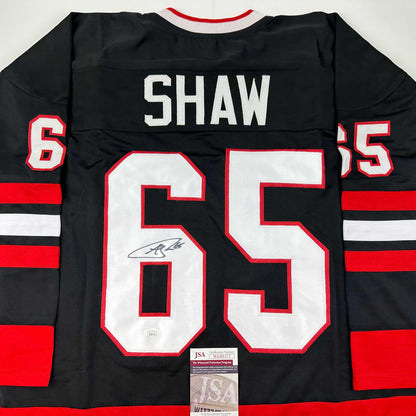 Back view of black and red striped hockey jersey displaying "SHAW" and number "65" with autographed signature and JSA authentication sticker.