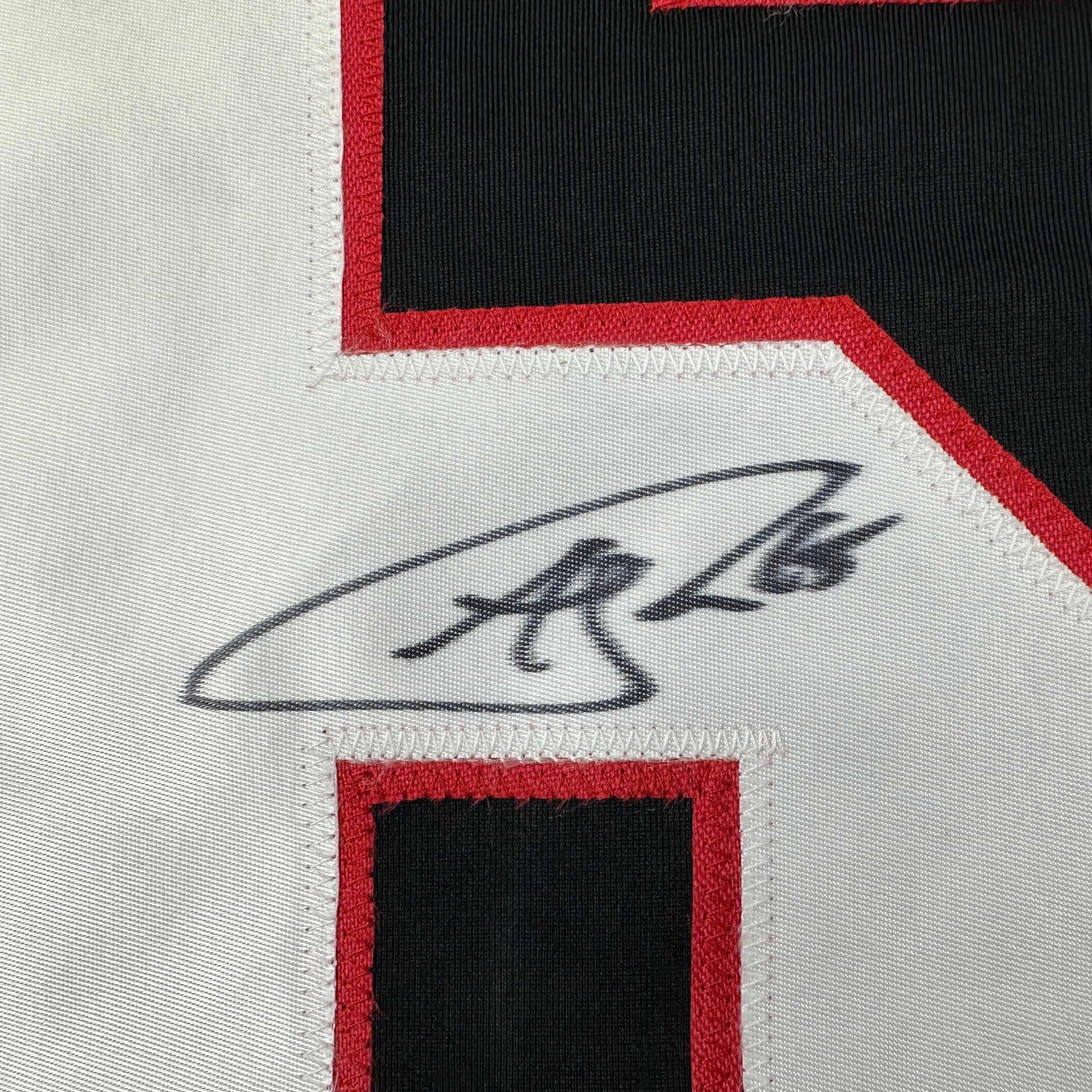 Close-up of Andrew Shaw's handwritten signature in black ink on white jersey fabric with red and black trim borders.