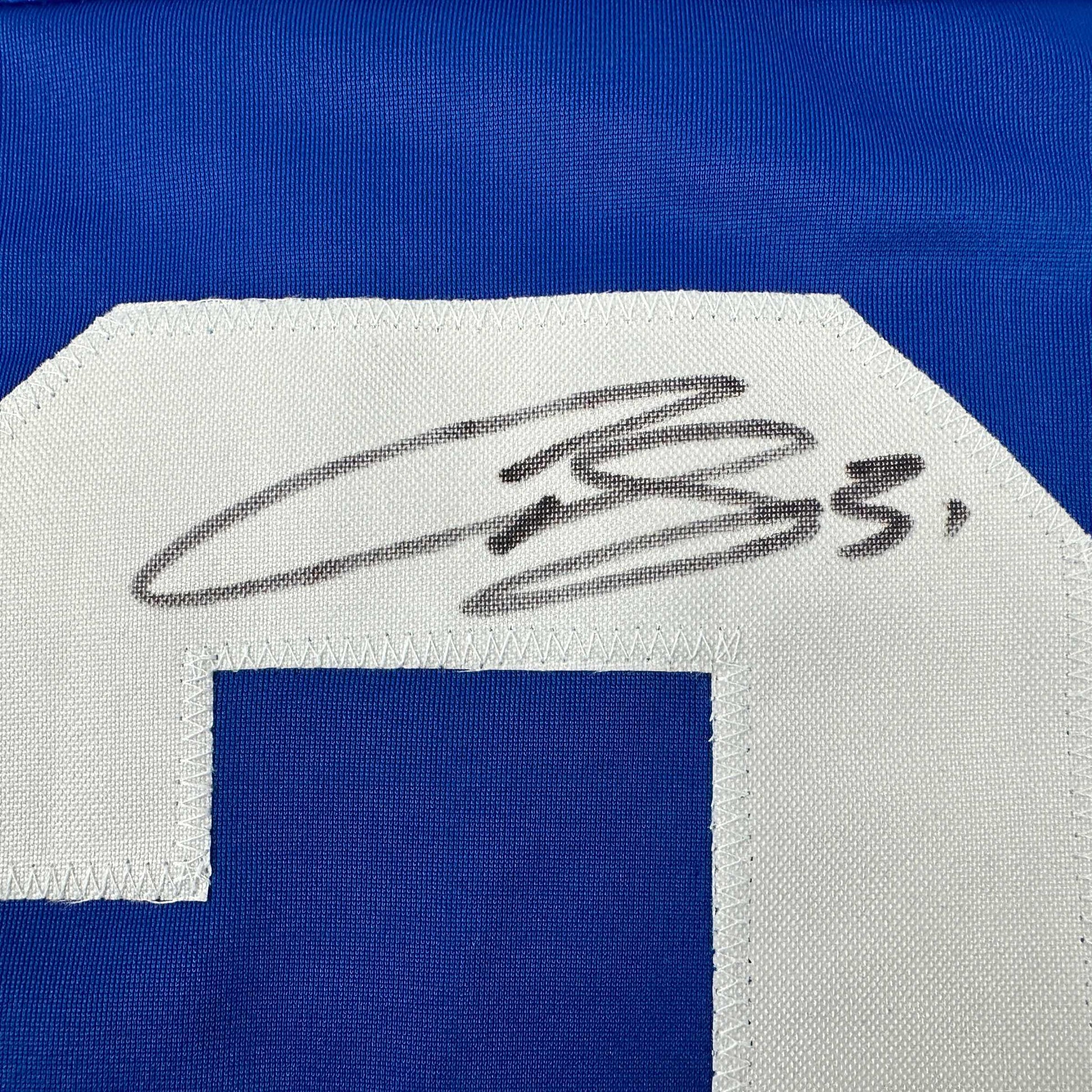 Close-up of handwritten signature in black ink on white fabric patch of blue hockey jersey.