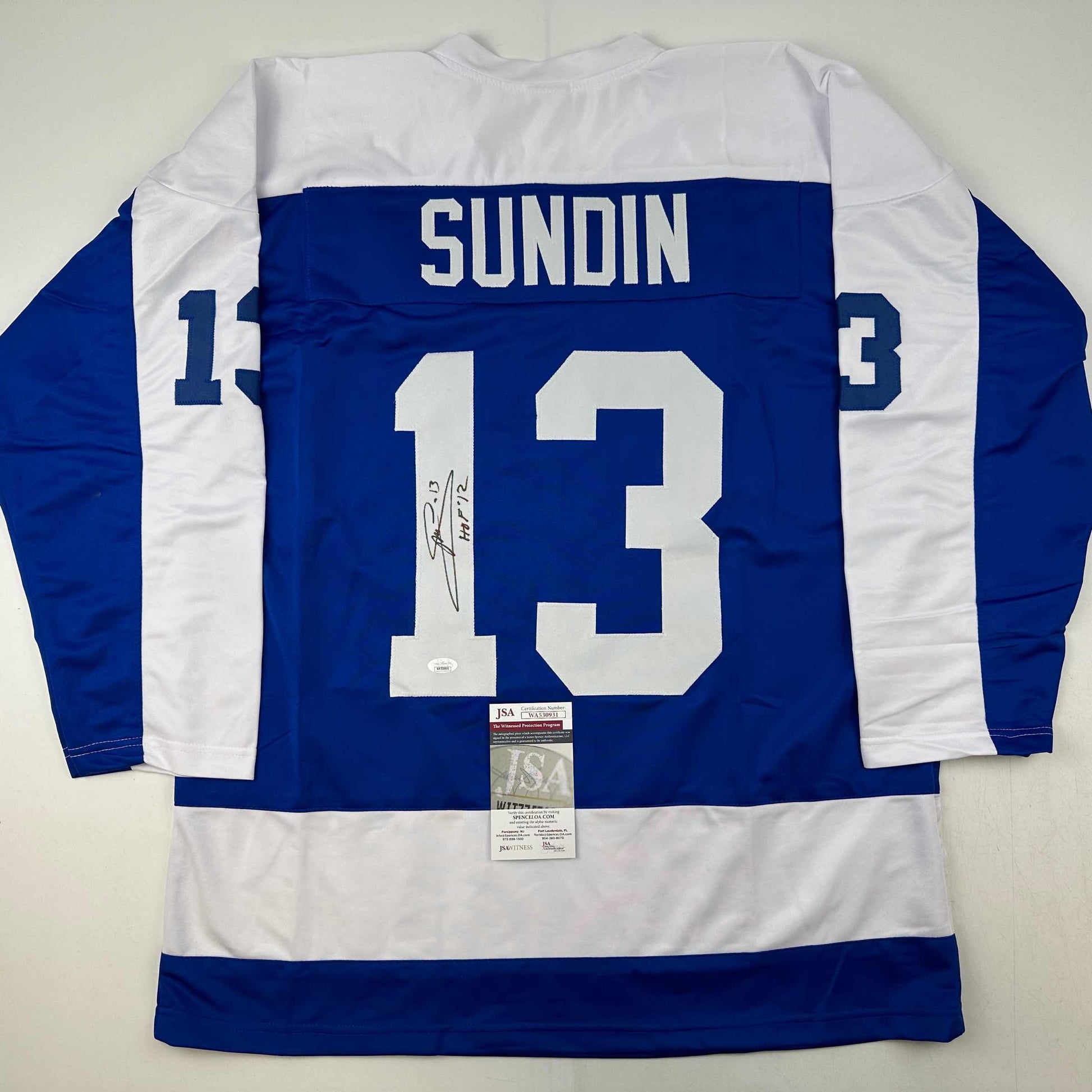 Back view of blue and white striped hockey jersey number 13 with "SUNDIN" nameplate and autographed signature, JSA authentication certificate visible.