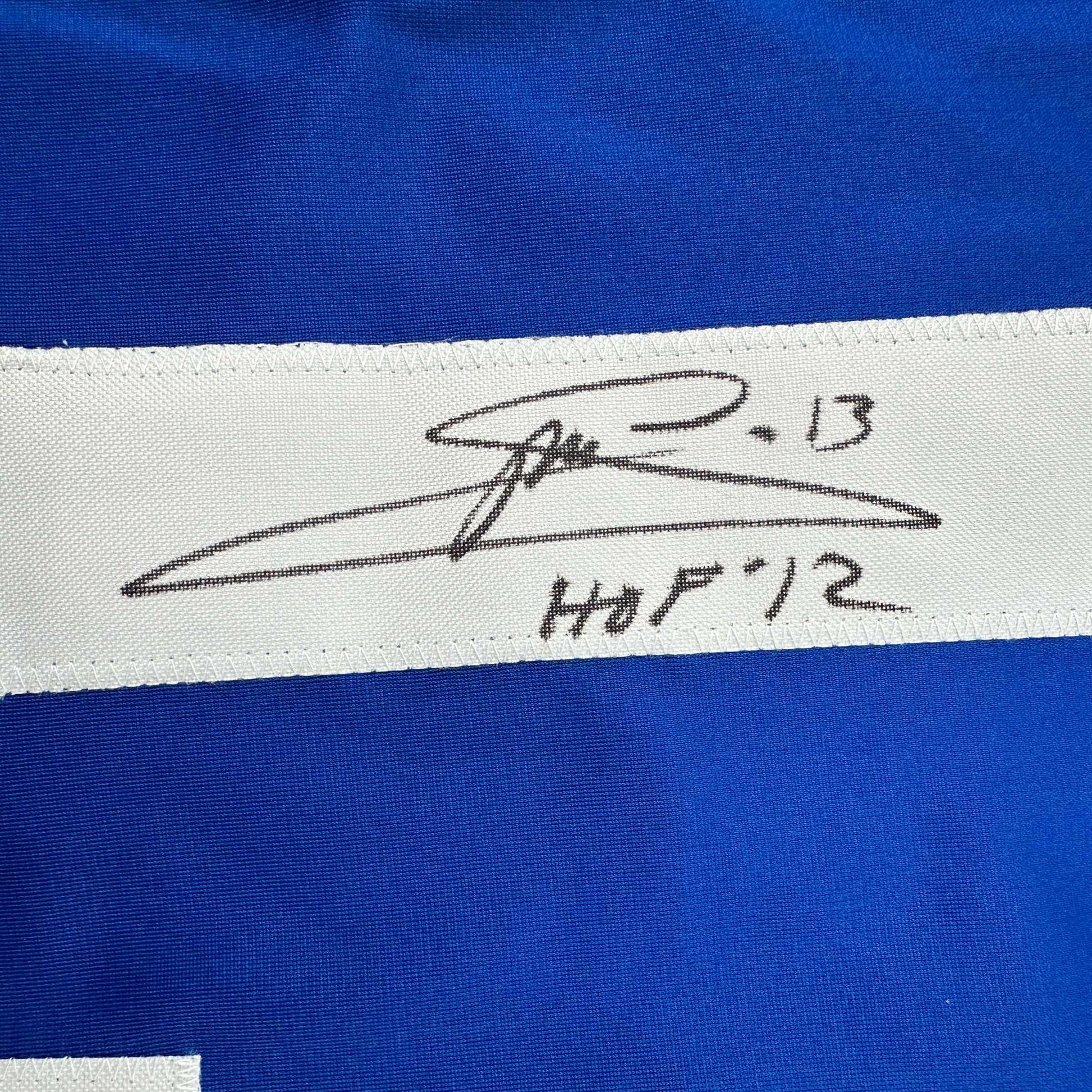 Close-up of handwritten signature and "HOF '12" on white stripe of blue hockey jersey.