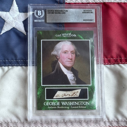 Front view of a graded slab holding a green-bordered card with a painted Washington portrait and handwriting clipping, on a flag.