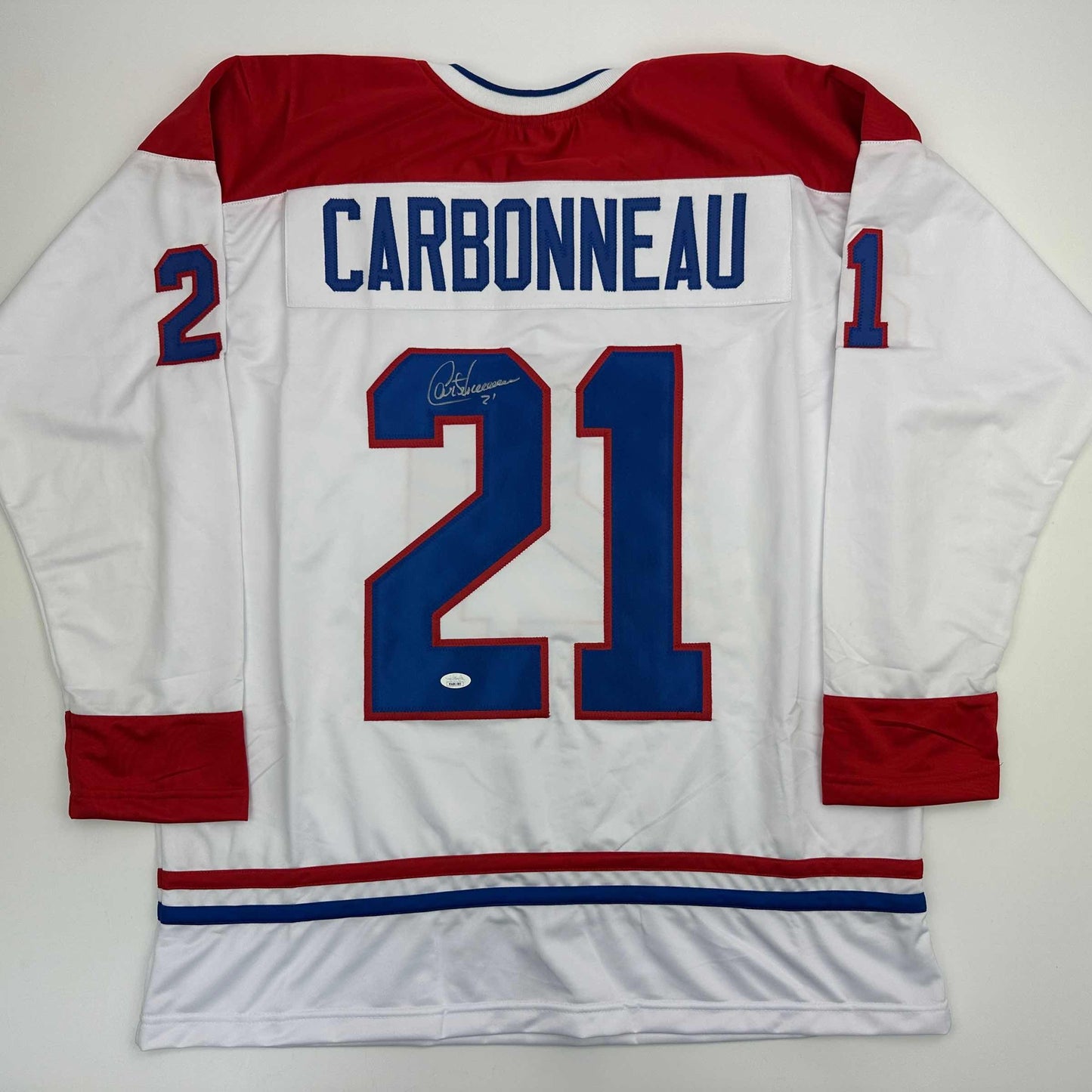 Autographed Montreal Canadiens jersey number 21 displaying Carbonneau nameplate, white body with red and blue trim, flat lay back view.