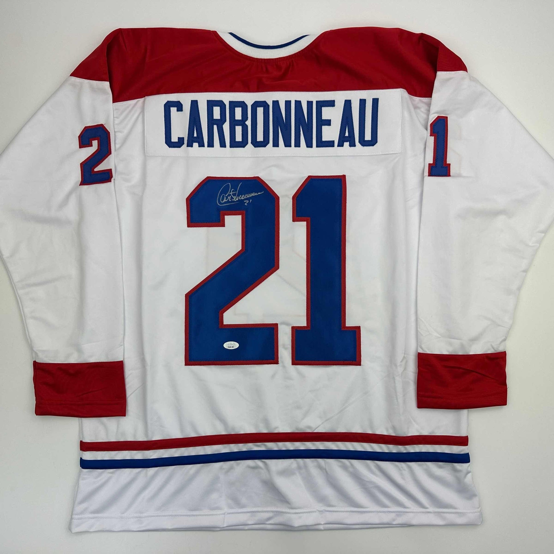 Autographed Montreal Canadiens jersey number 21 displaying Carbonneau nameplate, white body with red and blue trim, flat lay back view.