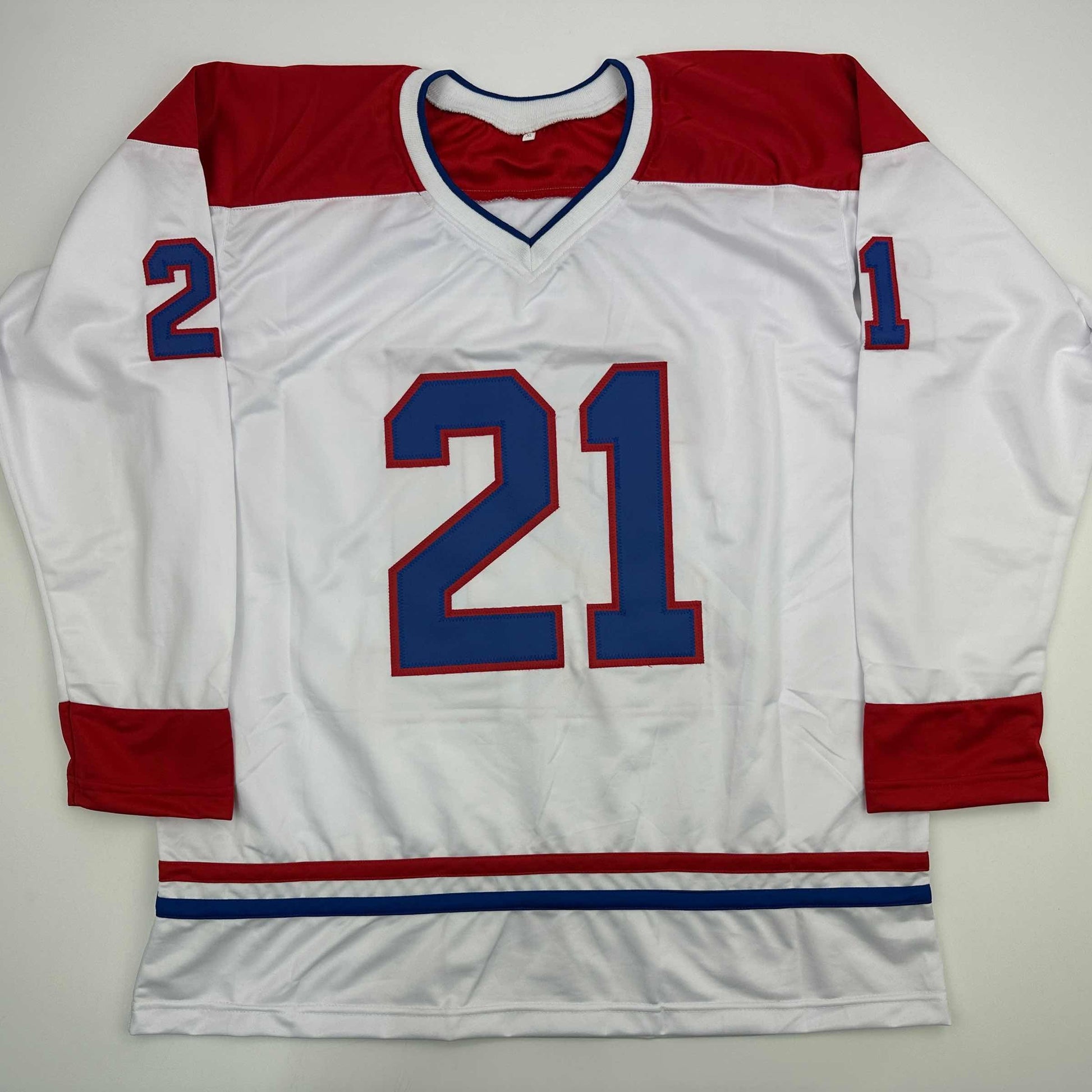 White Montreal Canadiens hockey jersey number 21 with red and blue trim displayed flat against gray background.