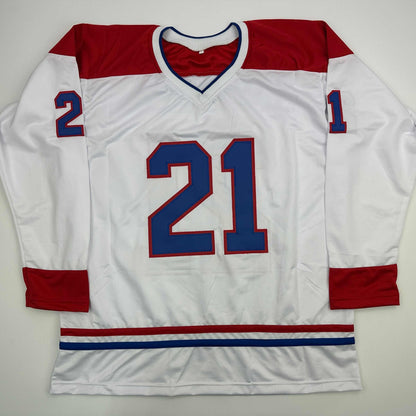 White Montreal Canadiens hockey jersey number 21 with red and blue trim displayed flat against gray background.