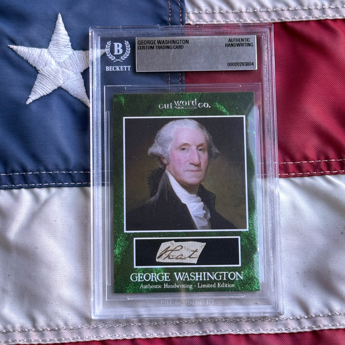 Front view of a Beckett slab resting on a flag, showing a green card with a portrait and a cut handwriting sample.