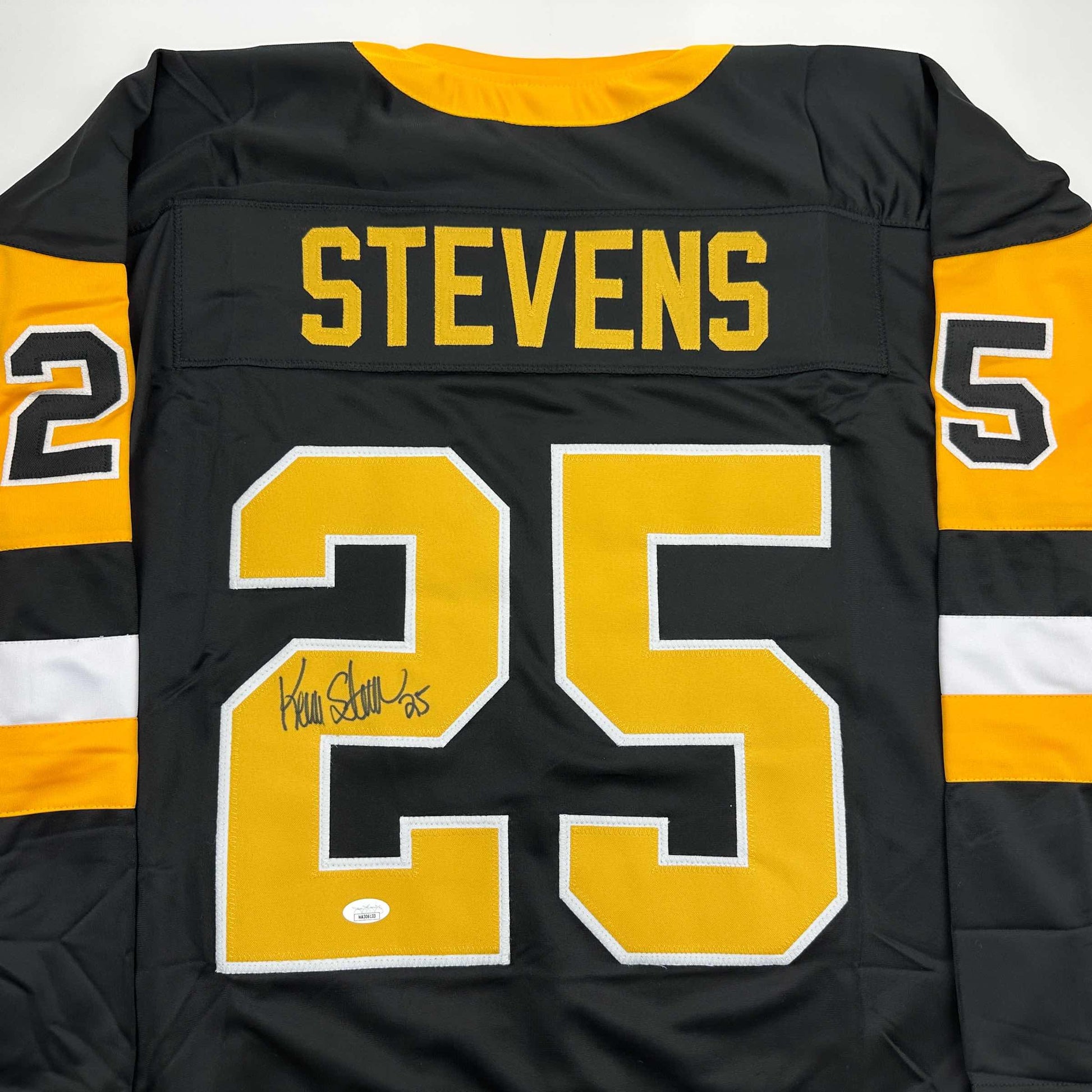 Front view of black and gold Pittsburgh hockey jersey number 25 with "STEVENS" nameplate and handwritten autograph on yellow number.
