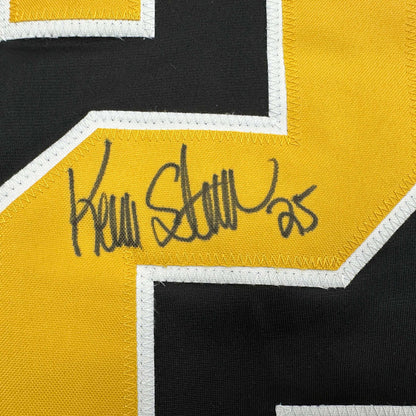 Close-up of Kevin Stevens's handwritten signature in black ink on yellow stripe of black and yellow hockey jersey.