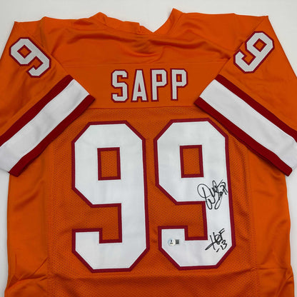 Close-up of the back of an orange football jersey, showing a white SAPP nameplate, number 99, and a black ink signature.