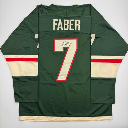 Back view of signed green hockey jersey with "FABER" and number 7 in red and cream, displaying signature on number.