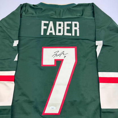 Back view of green Minnesota hockey jersey number 7 with "FABER" nameplate and handwritten signature on white number.