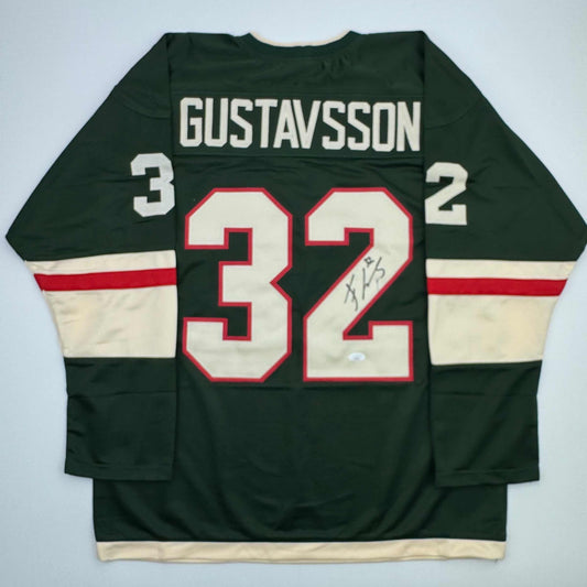 Back view of dark green hockey jersey with white "GUSTAVSSON" nameplate and number 32 with autograph, cream and red horizontal stripes on sleeves.