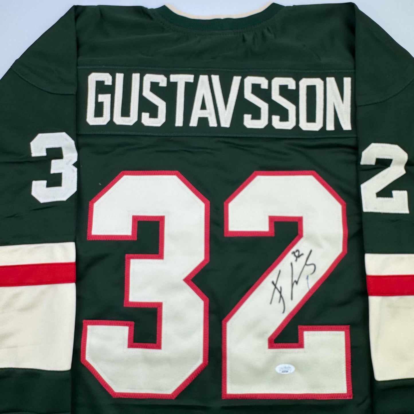 Back view of dark green hockey jersey with "GUSTAVSSON" and number 32 in red and white, featuring handwritten signature on the number.
