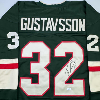 Back view of dark green hockey jersey with "GUSTAVSSON" and number 32 in red and white, featuring handwritten signature on the number.