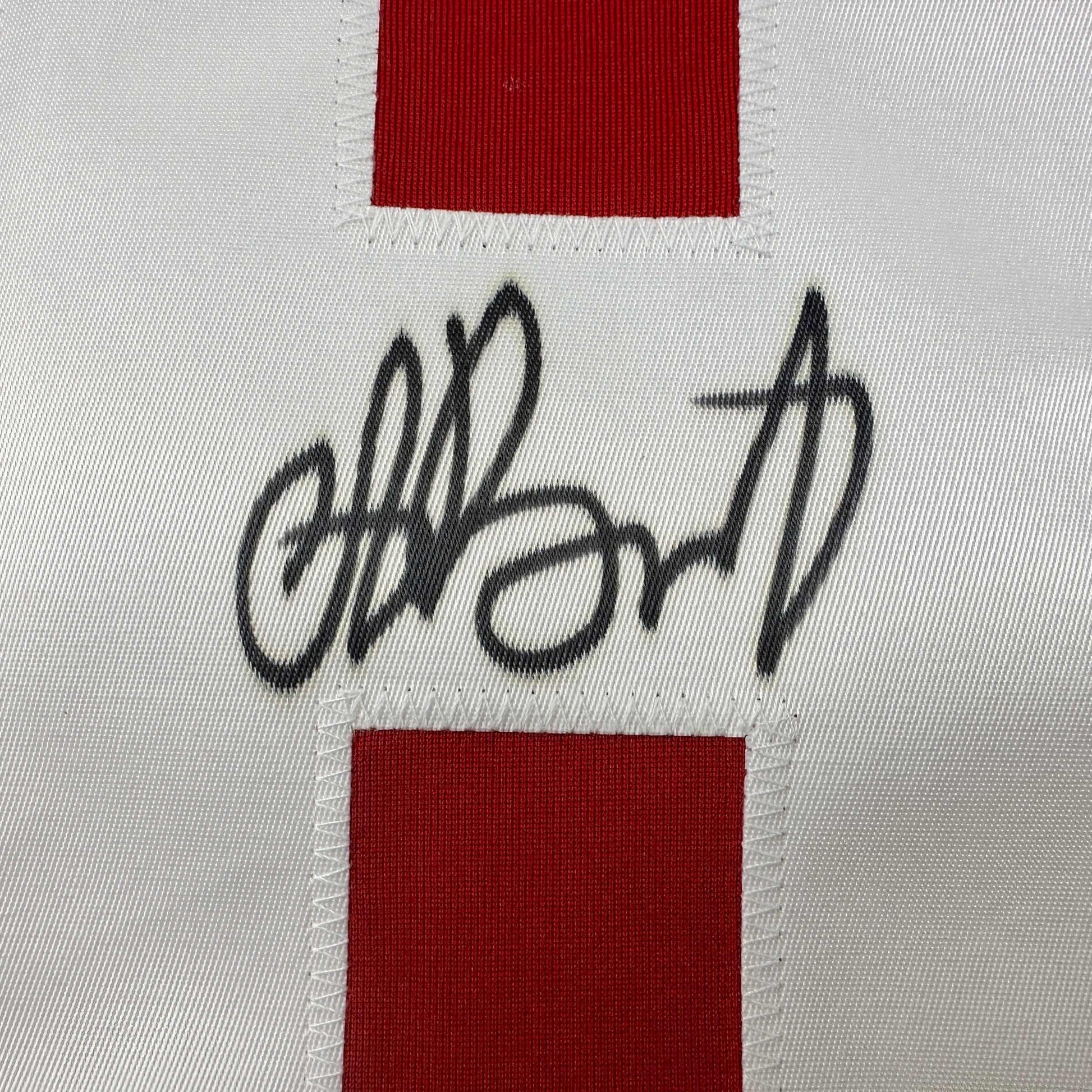 Close-up of handwritten black signature on white fabric between red horizontal stripes on hockey jersey.