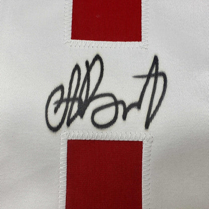Close-up of handwritten black signature on white fabric between red horizontal stripes on hockey jersey.