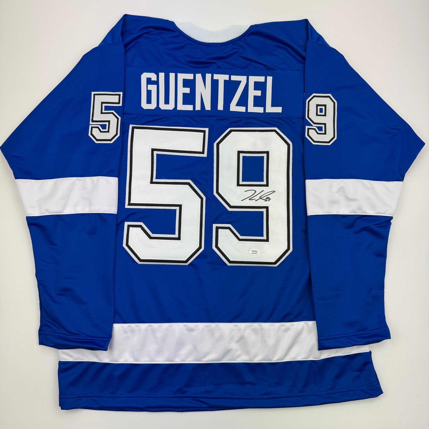 Back view of blue and white striped hockey jersey with "GUENTZEL 59" and autograph on white number, displayed flat against white background.