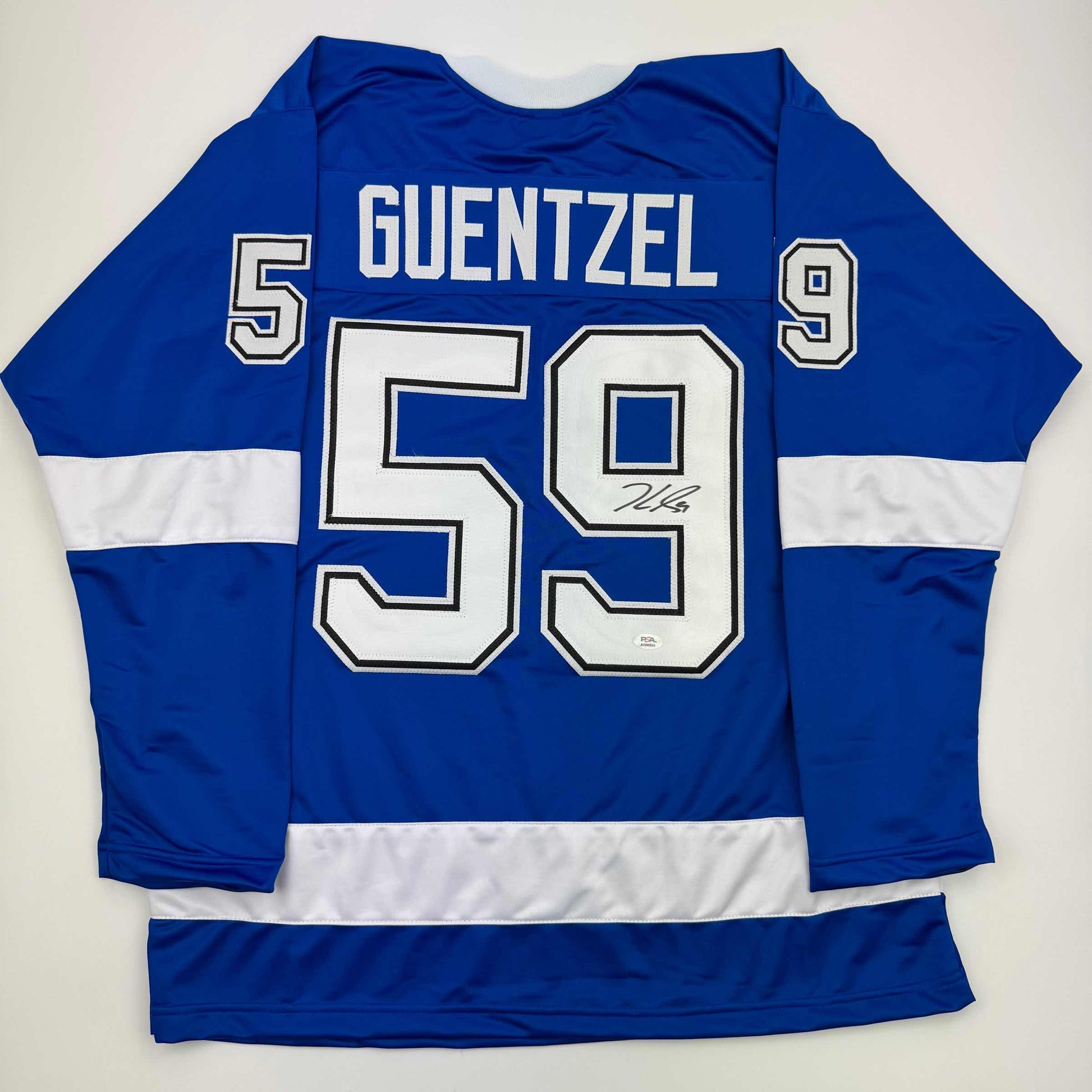 Back view of blue and white striped hockey jersey with "GUENTZEL 59" and autograph on white number, displayed flat against white background.