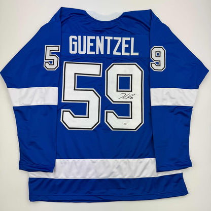 Back view of blue and white striped hockey jersey with "GUENTZEL 59" and autograph on white number, displayed flat against white background.
