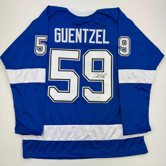 Back view of blue and white striped hockey jersey with "GUENTZEL 59" and autograph on white number, displayed flat against white background.