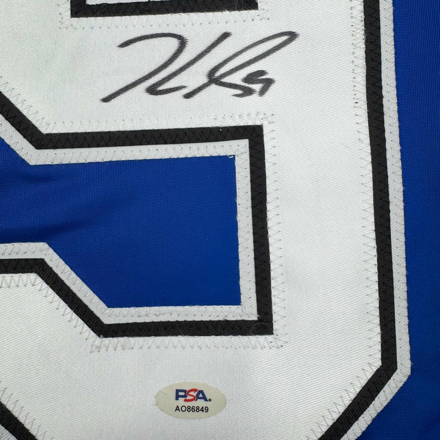 Close-up of autographed Jake Guentzel jersey showing handwritten signature on white panel with blue and black geometric design and PSA authentication sticker.