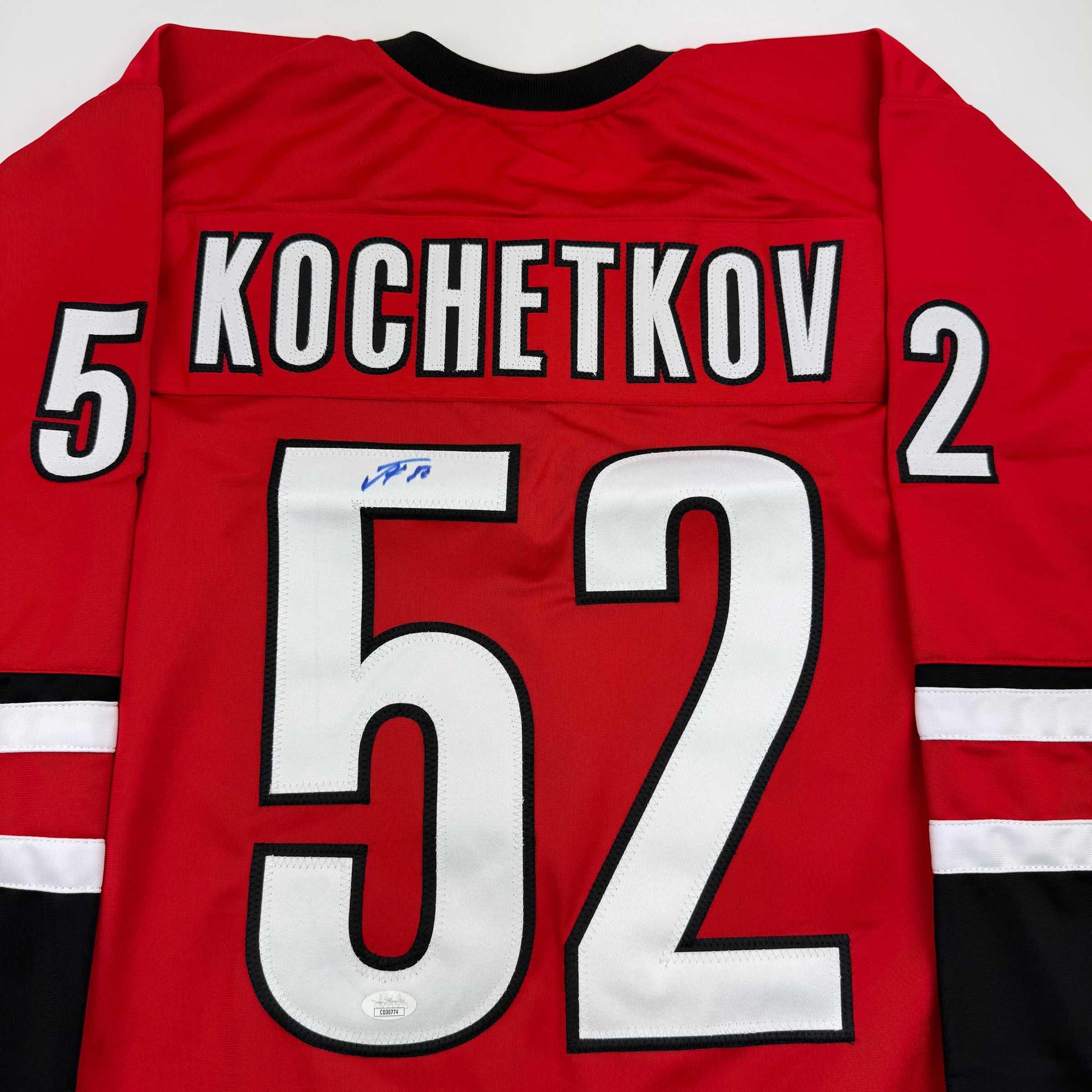 Red Carolina hockey jersey with white and black "KOCHETKOV" nameplate and number "52" on back, blue autograph visible on chest.