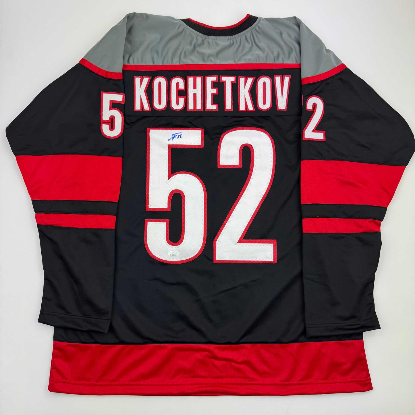 Back view of black, red, and gray hockey jersey displaying "KOCHETKOV" and number 52 in white and red lettering.