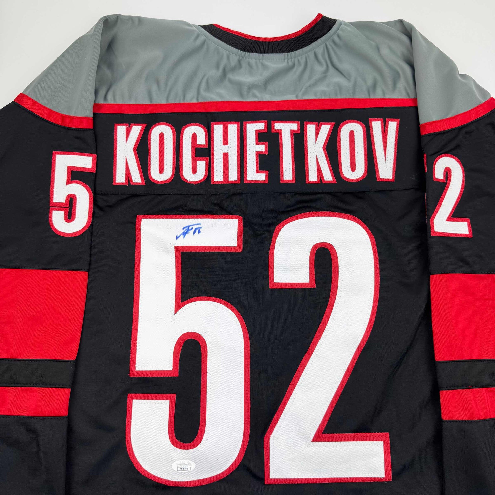 Back view of black and red striped hockey jersey with "KOCHETKOV" and number 52 printed across shoulders, large number 59 on back, and autograph visible on white number.