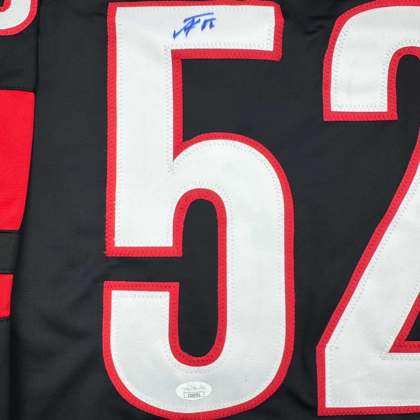 Close-up of number 52 in white with red trim on black hockey jersey, with blue autograph on upper white section.
