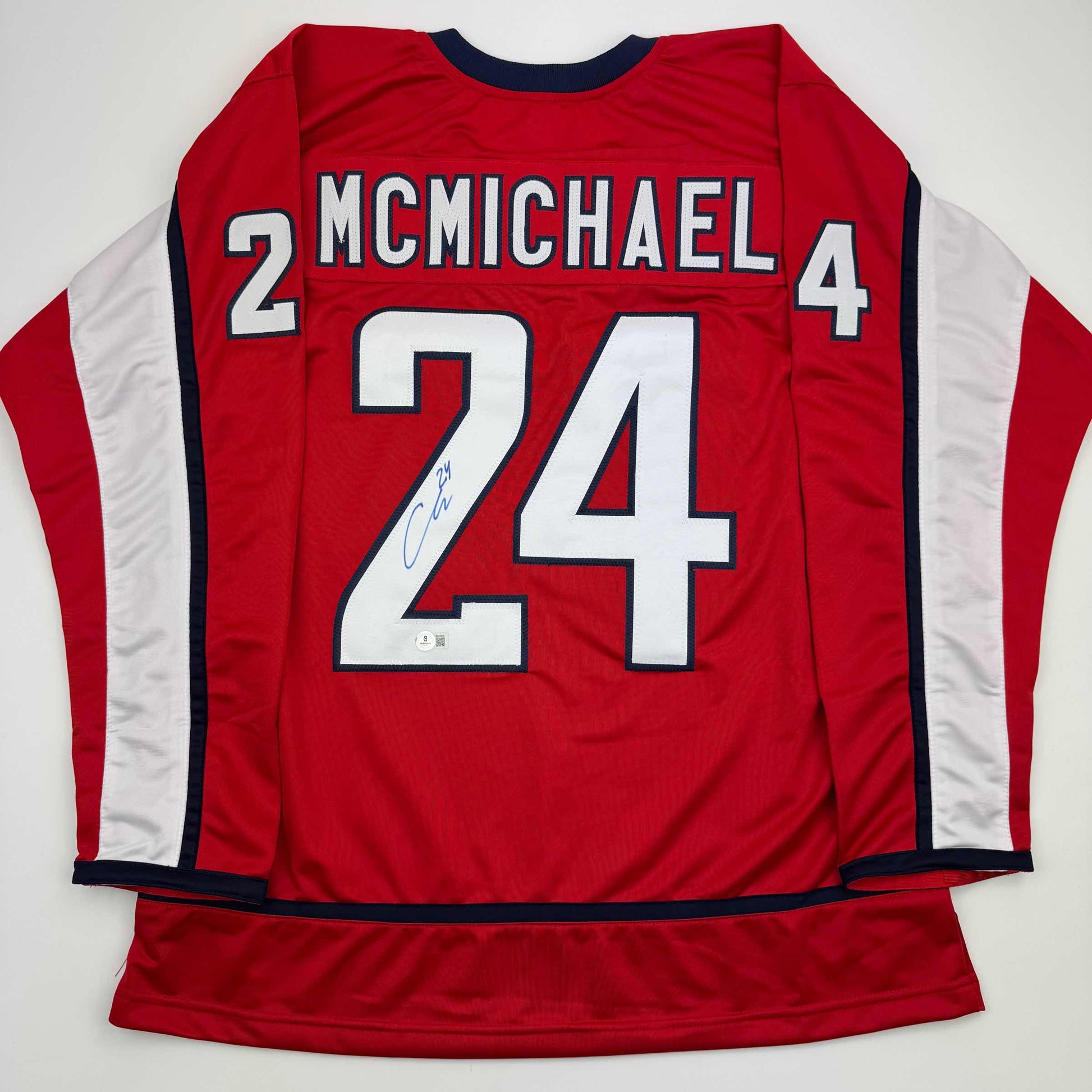 Back view of red hockey jersey with white number 24, "MCMICHAEL" nameplate, white side panels, and blue neckline trim.