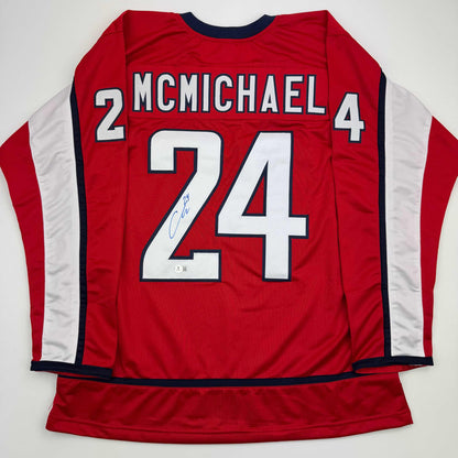 Back view of red hockey jersey with white number 24, "MCMICHAEL" nameplate, white side panels, and blue neckline trim.
