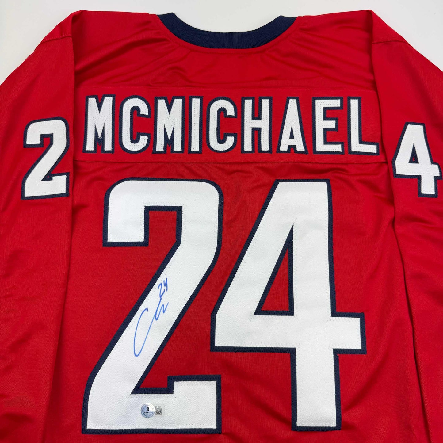 Red hockey jersey back view showing "MCMICHAEL" name and number 24 with blue autographed signature on white number.