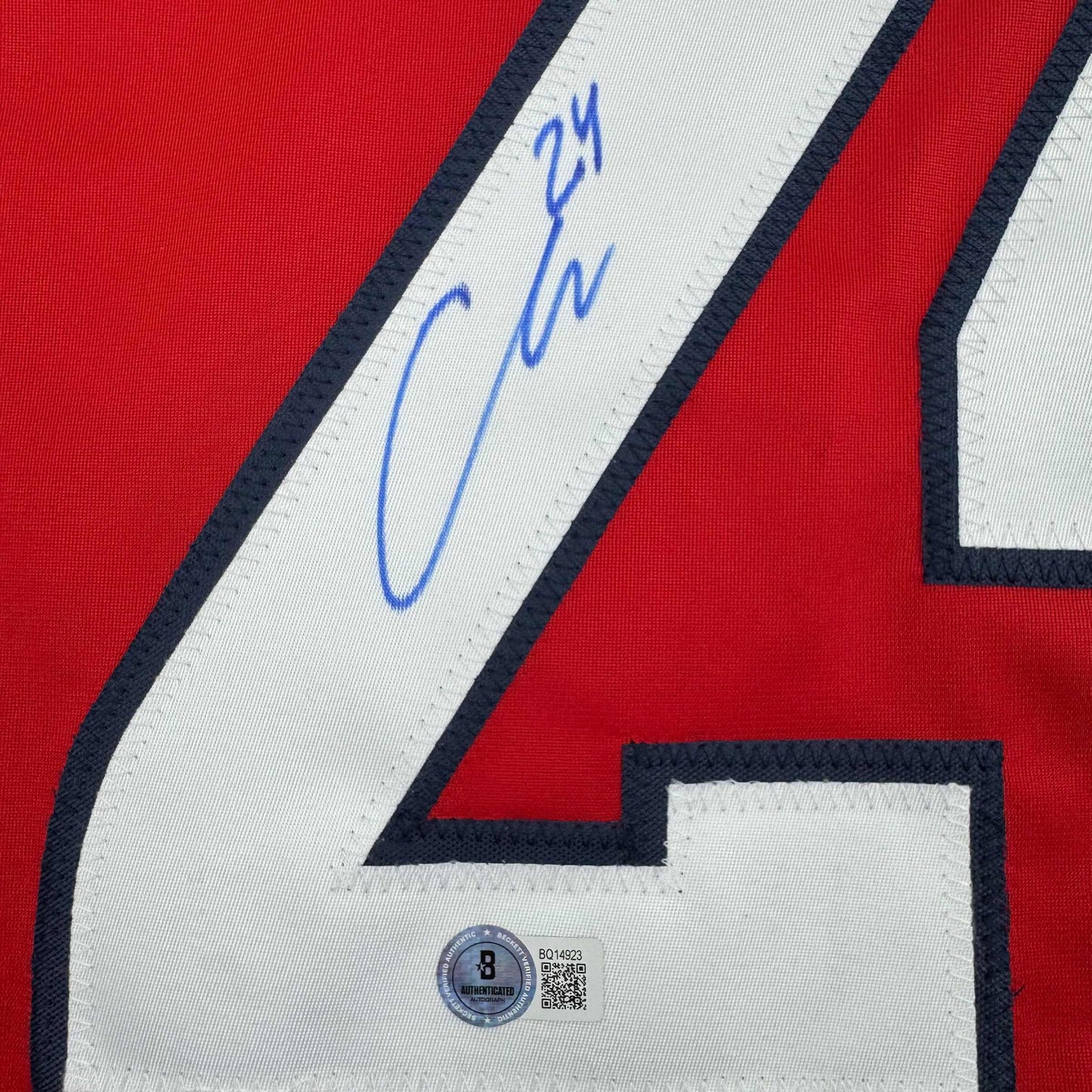 Close-up of signed red hockey jersey white stripe with blue autograph and Beckett authentication hologram visible.