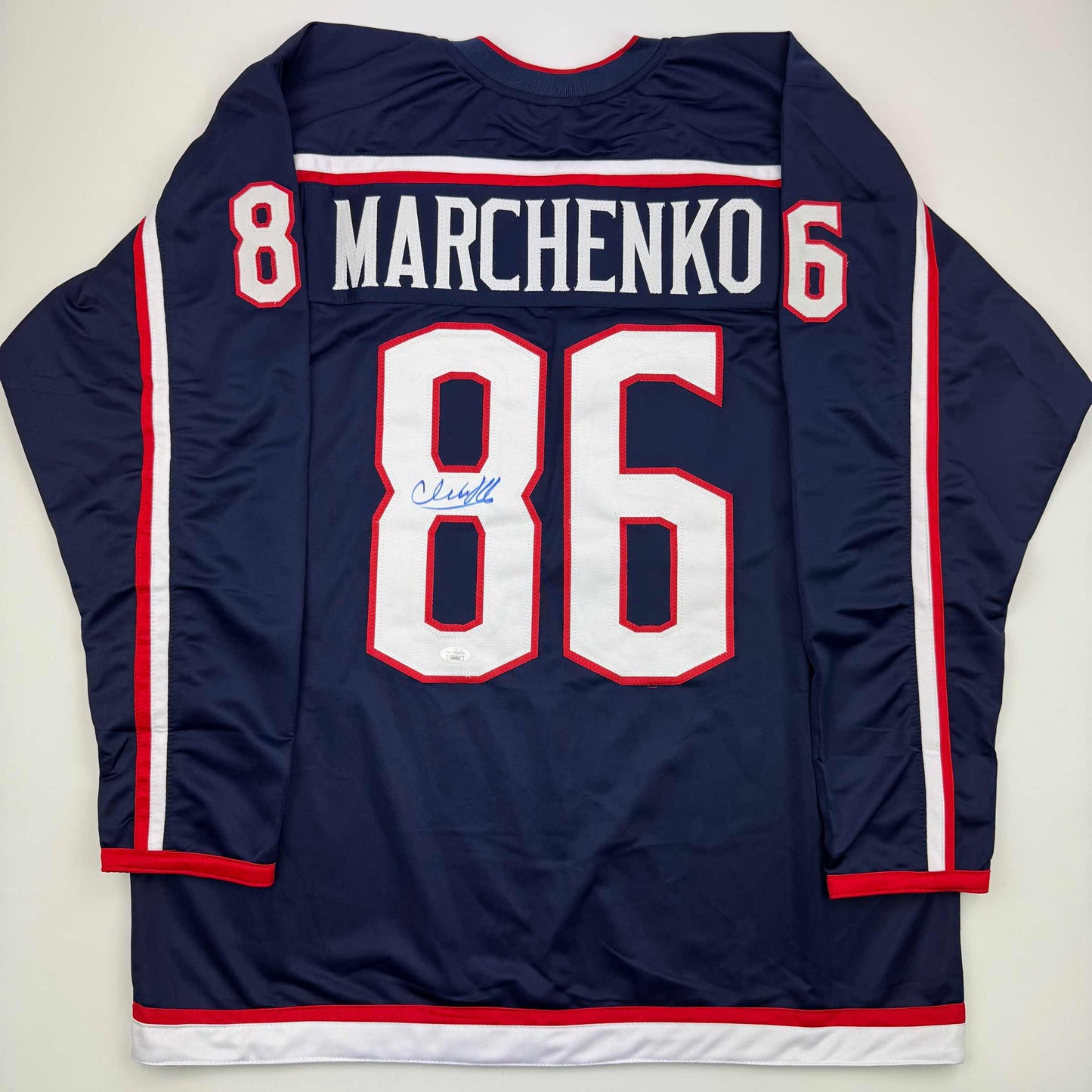 Back view of navy blue hockey jersey with "MARCHENKO" and number 86 in white and red lettering, featuring autographed signature on chest.
