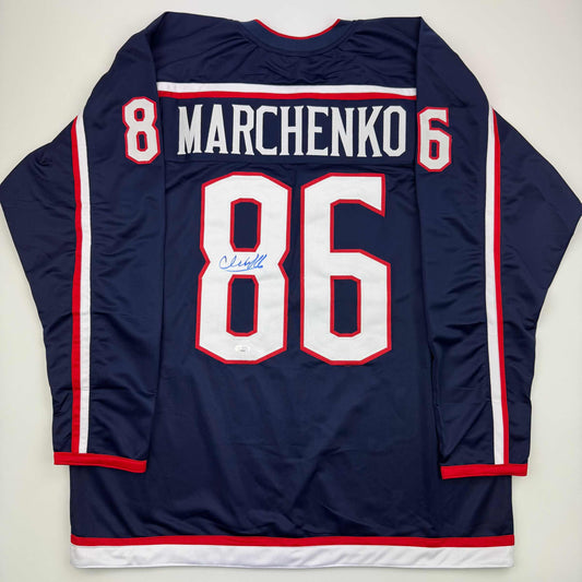 Back view of navy blue hockey jersey with "MARCHENKO" and number 86 in white and red lettering, featuring autographed signature on chest.