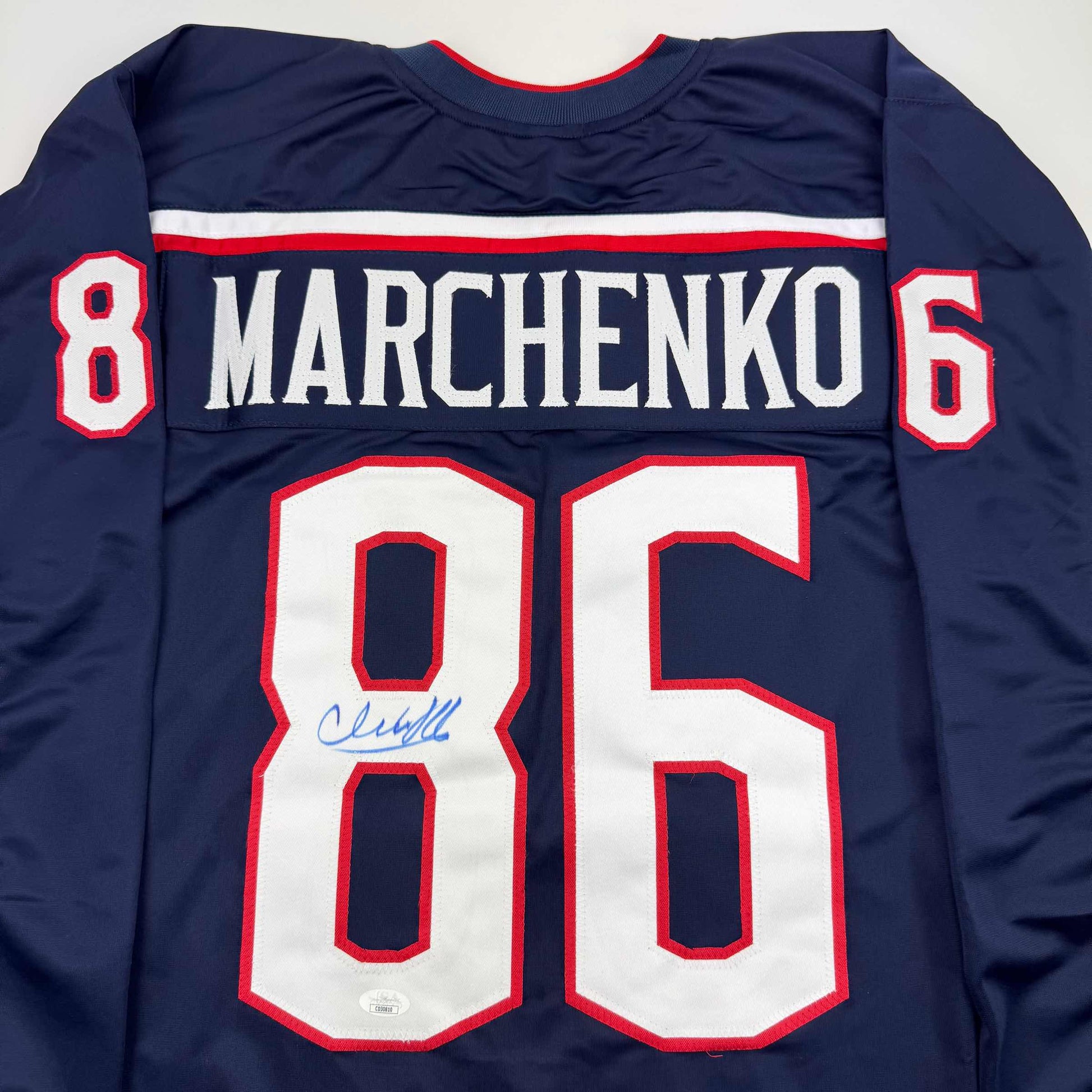 Navy blue hockey jersey with red and white trim displaying "MARCHENKO" and number 86, with autographed number 8 visible on front.