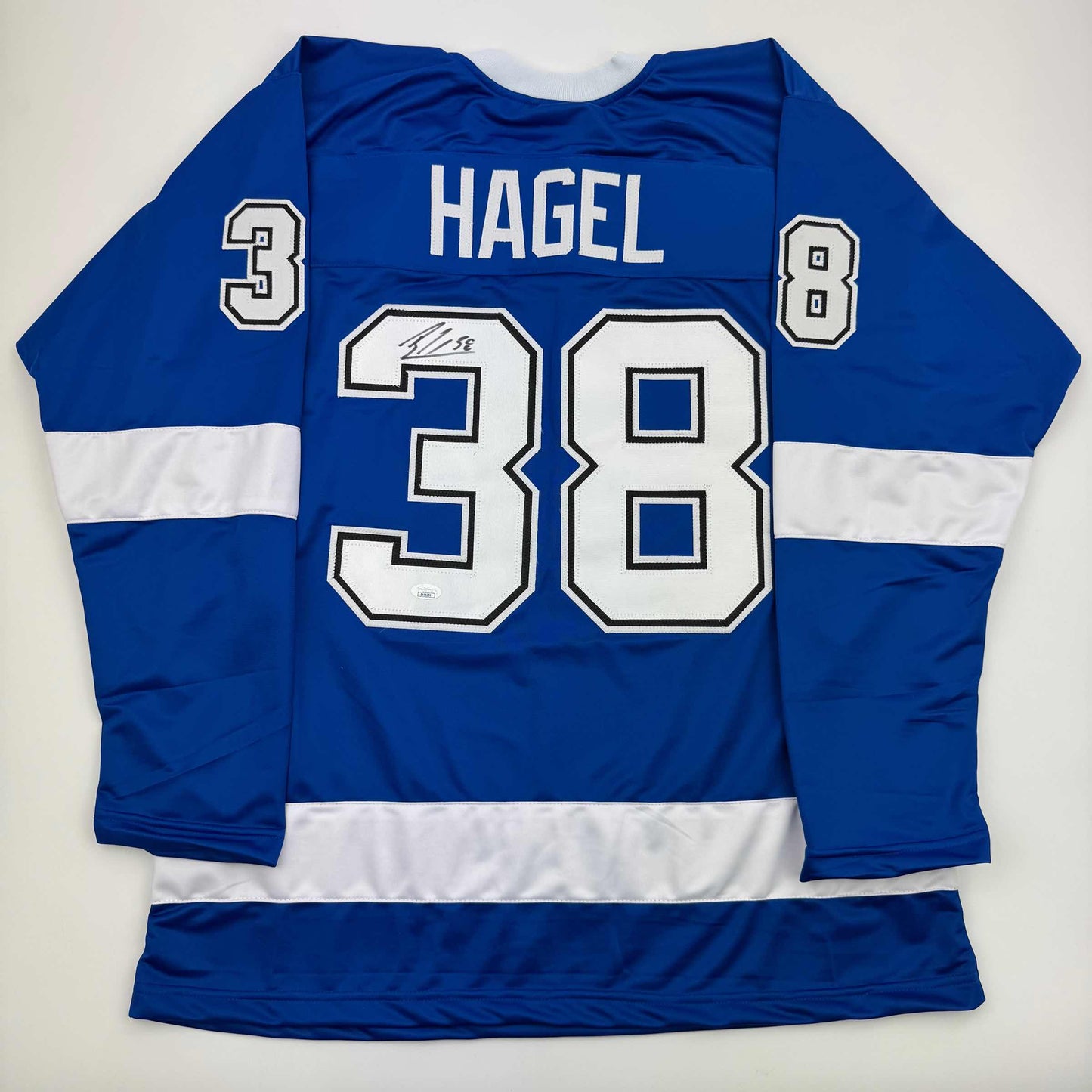 Blue and white striped hockey jersey displaying "HAGEL" and number 38 on back, laid flat on white background.