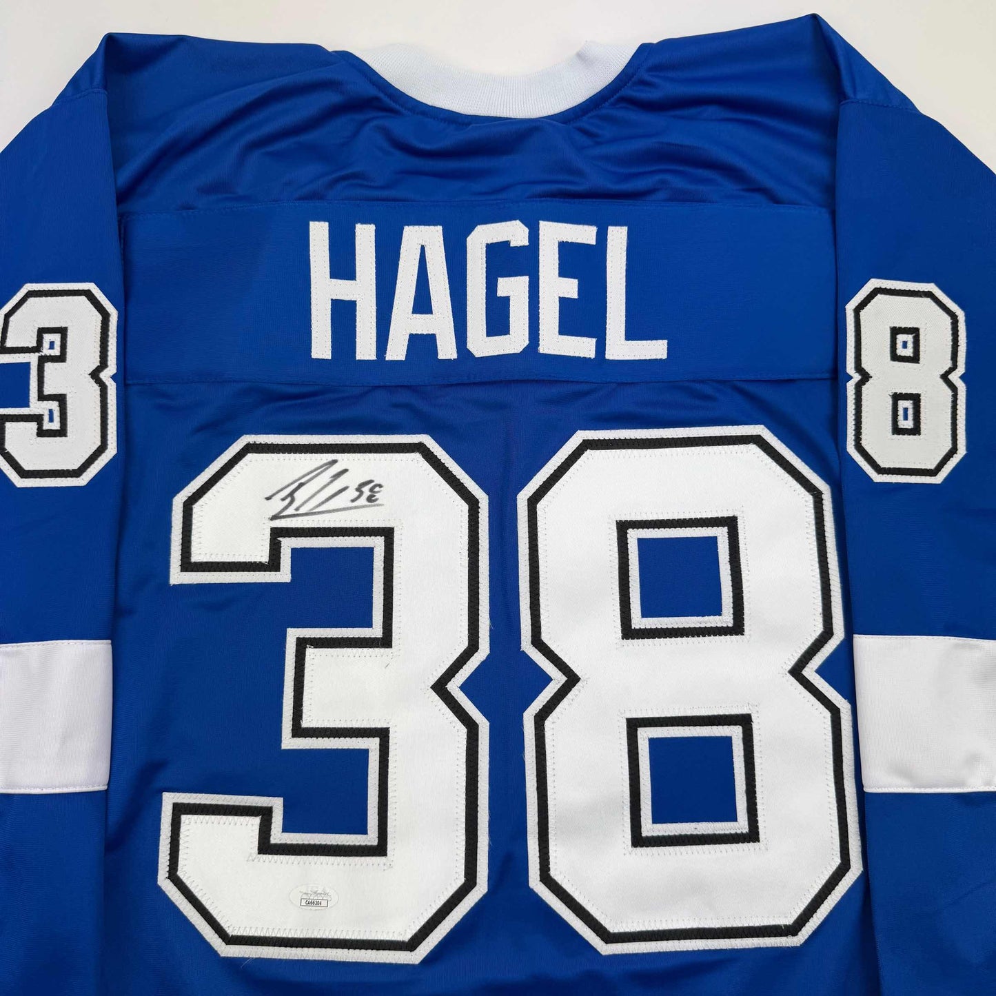 Back view of blue hockey jersey with "HAGEL" and number 38 in white, featuring autographed number 39 patch.