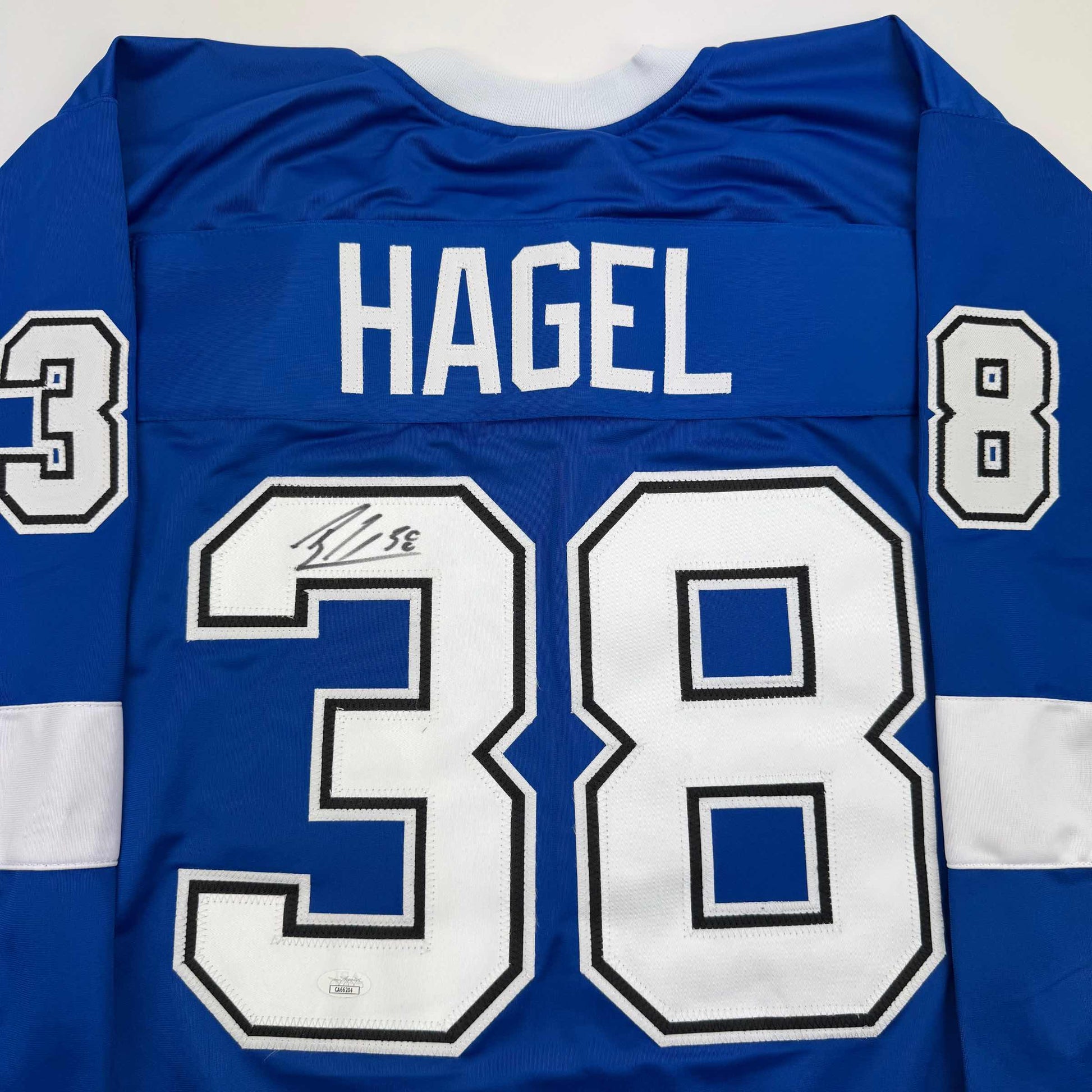 Back view of blue hockey jersey with "HAGEL" and number 38 in white, featuring autographed number 39 patch.