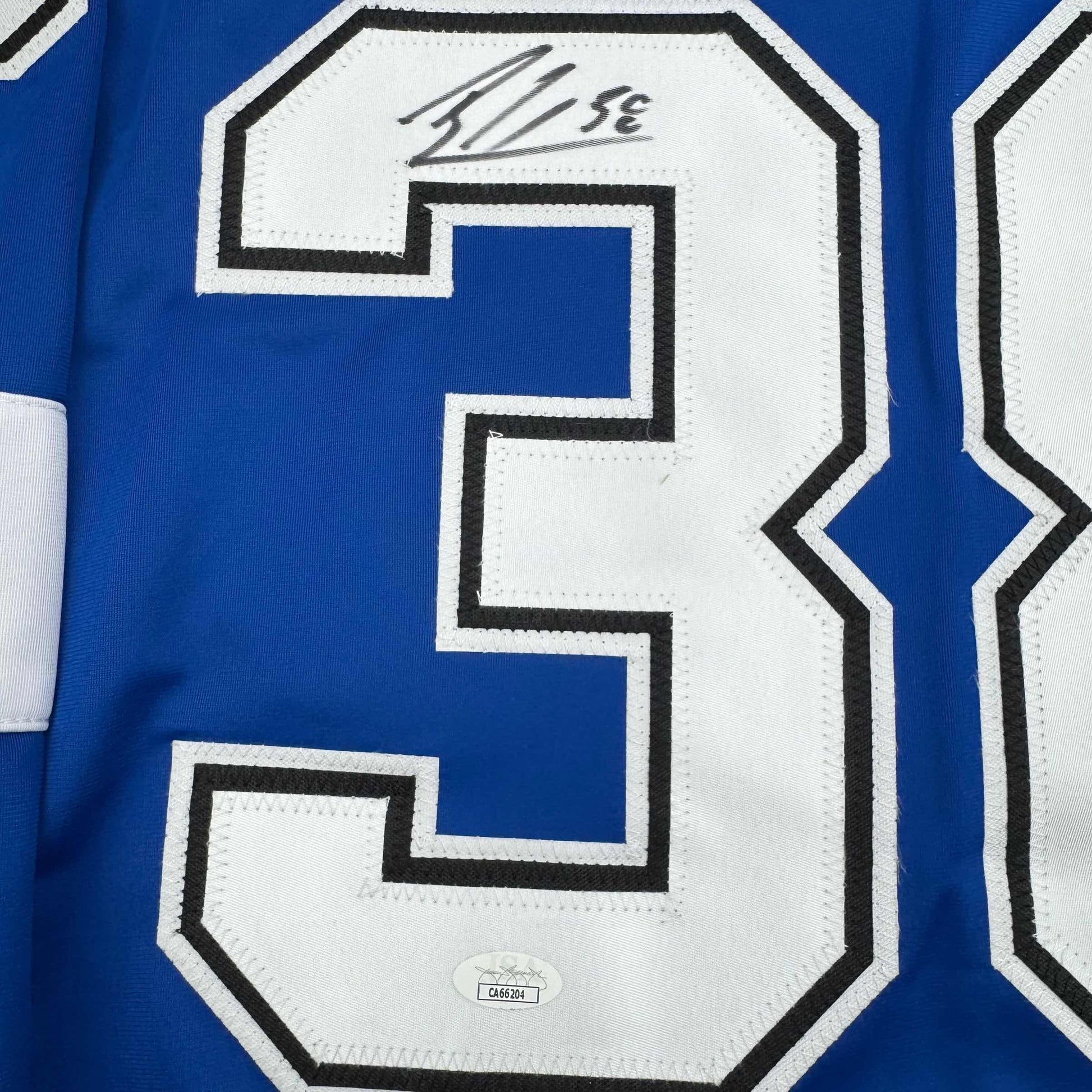 Close-up of blue hockey jersey number 3 with white and black stitching, showing autograph and JSA authentication hologram.