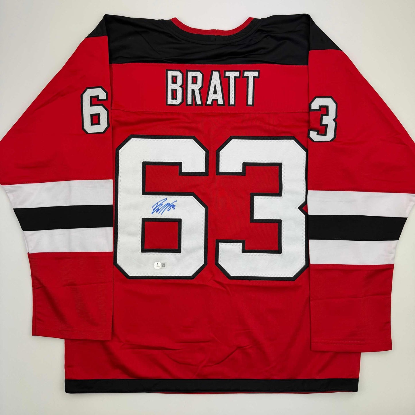Red hockey jersey displayed flat showing back with "BRATT" nameplate, number 63, and blue autograph on white number.