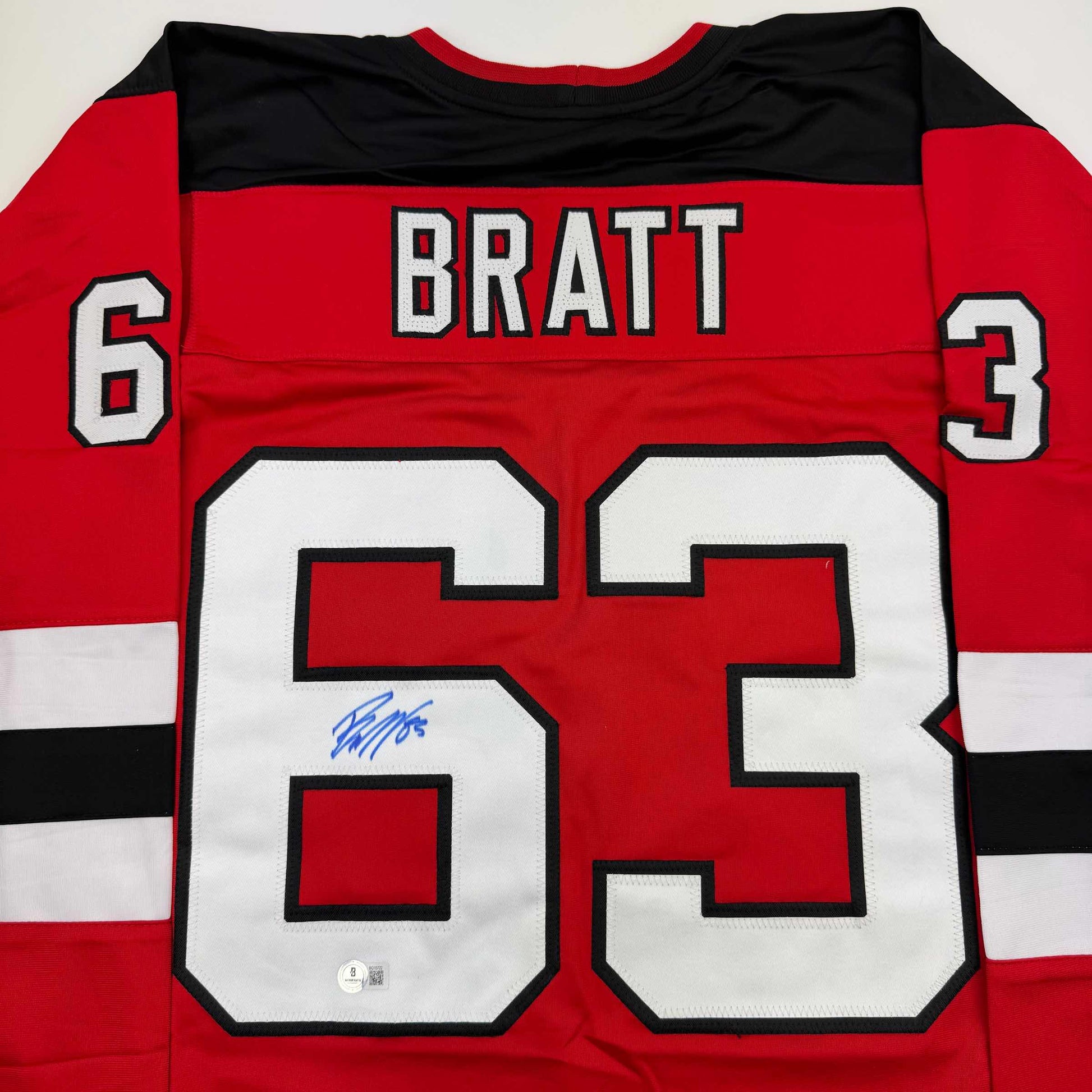 Red hockey jersey front view displaying "BRATT" and number 63 in white with blue autograph on white number.